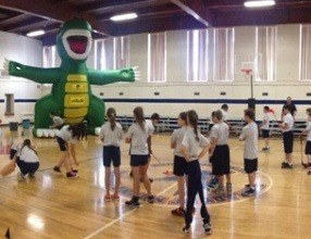 Children participating in golf activities beside a green Golfzilla inflatable target in a gym